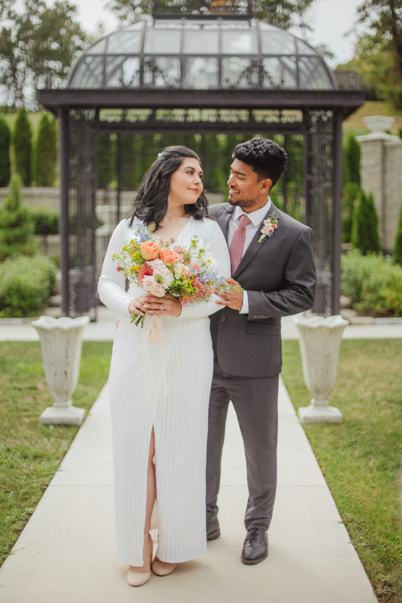 Bride and Groom looking at each other in front of a pavilion holding a bridal bouquet designed by St. Louis Wedding Florist, Suncrest Blooms.