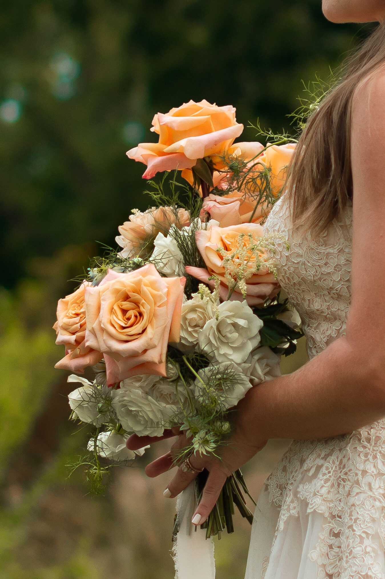 Bride holds a bouquet featuring peach roses and cream spray roses.
